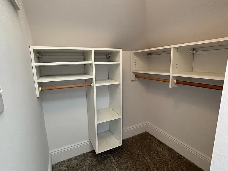 Empty white built-in closet with shelves and hanging rods in a small room.
