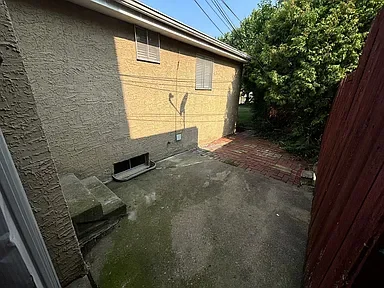 Backyard with concrete patio, brick path, and a large tree with green leaves, fenced by a wooden fence.