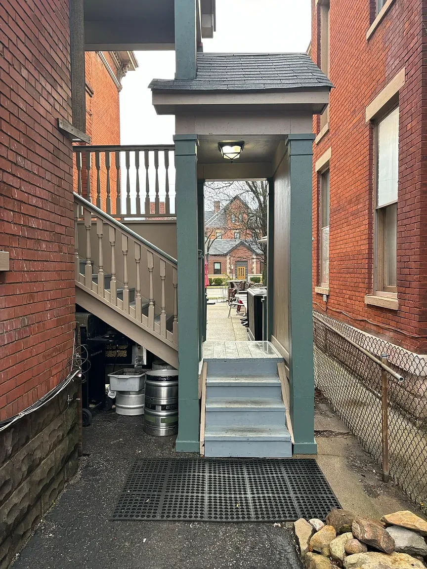 Back entrance of a brick building with a small covered porch, stairs leading up to it, and a lamp overhead.