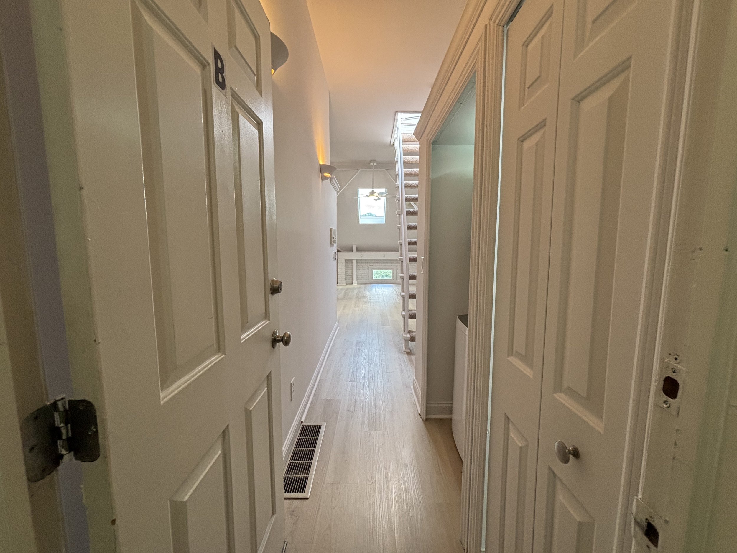 Interior view of a hallway leading to a staircase with railing, a window, and hardwood flooring.
