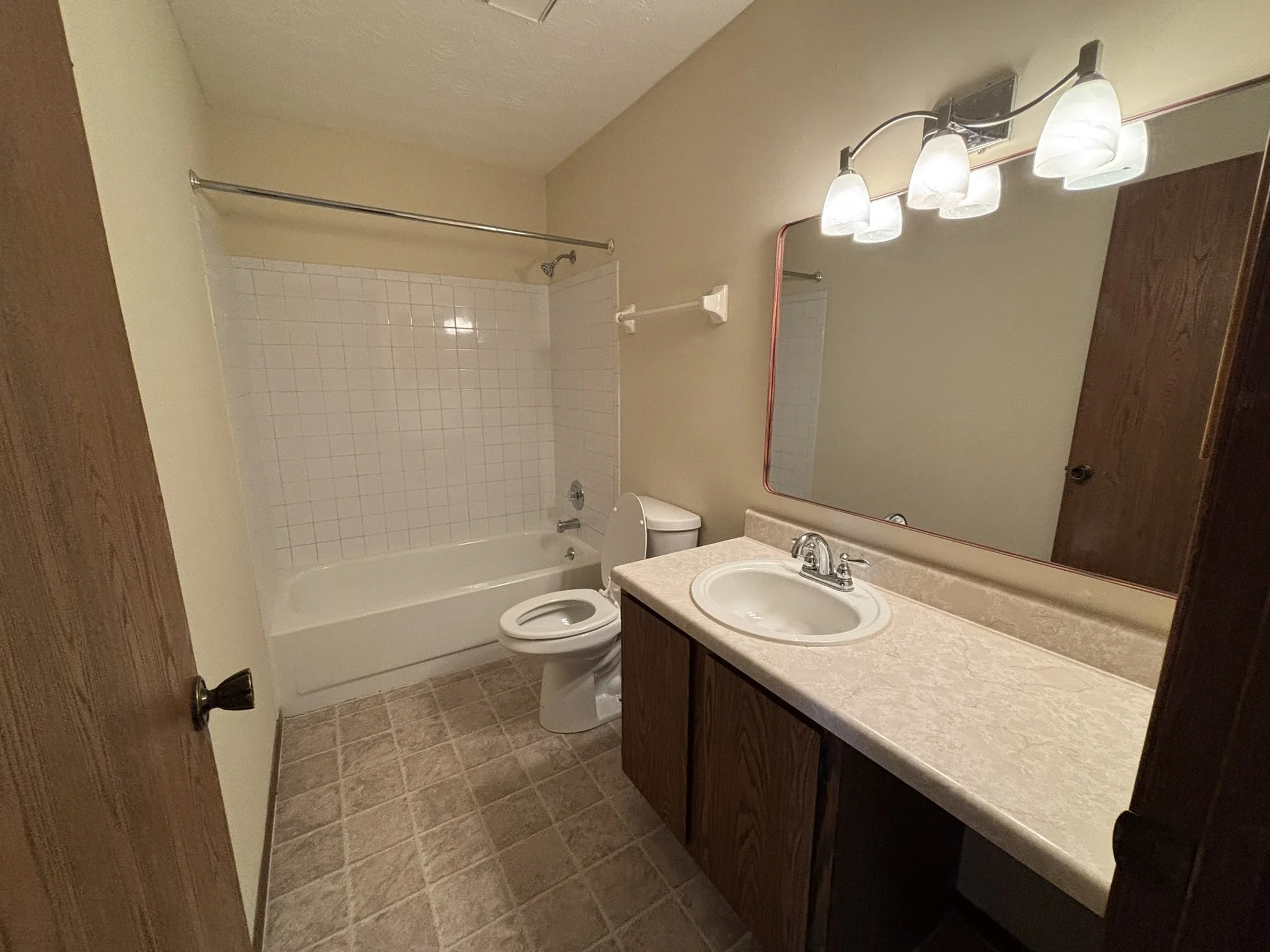 Bathroom with a bathtub and shower area, toilet, wooden vanity with a sink, mirror, and overhead light fixture.