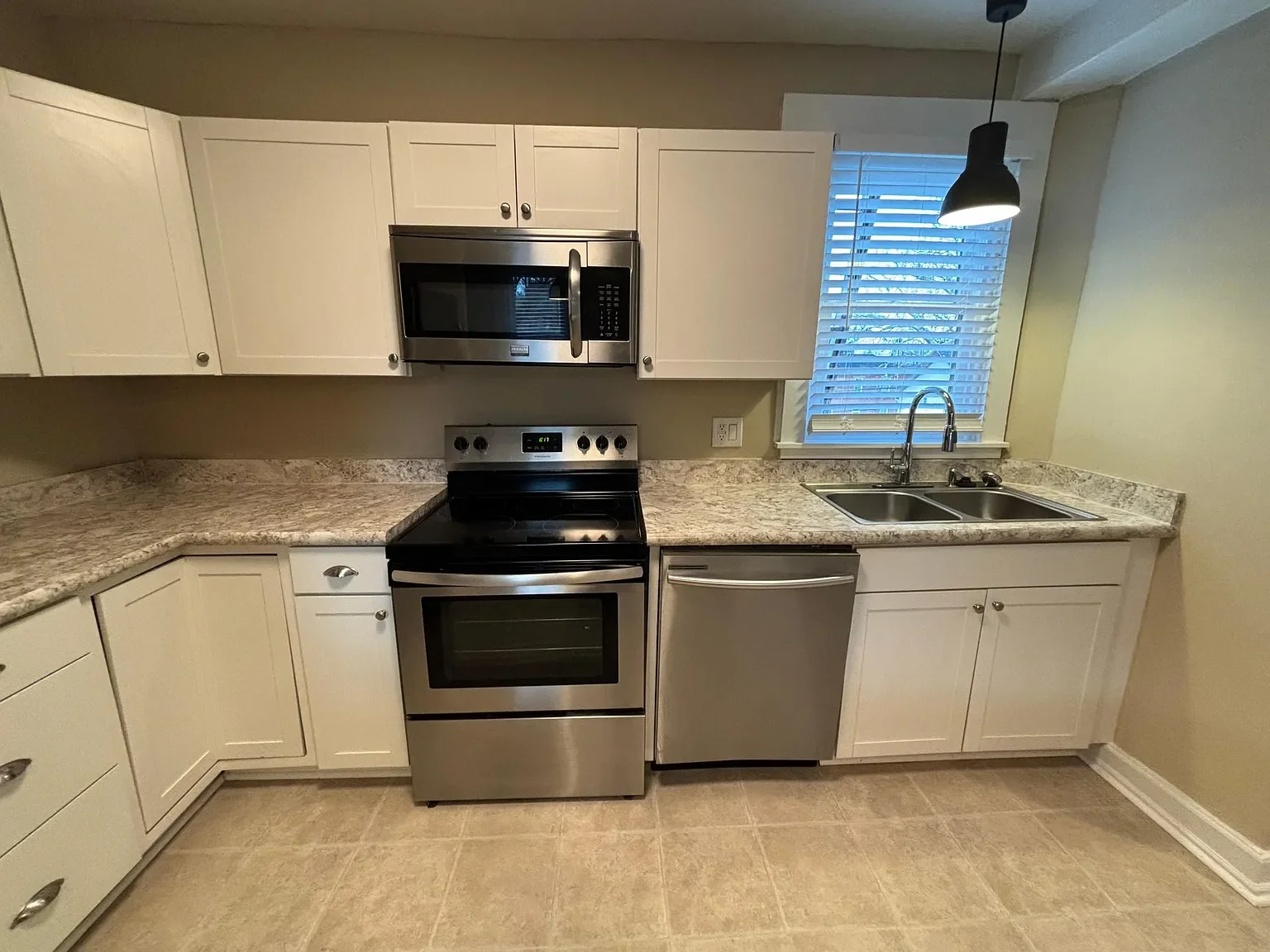Kitchen with white cabinets, stainless steel stove and microwave, granite countertops, a double sink, and a window with blinds