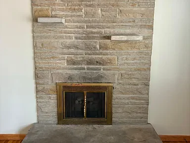 A stone fireplace with a glass door in a room with beige walls and wooden flooring.