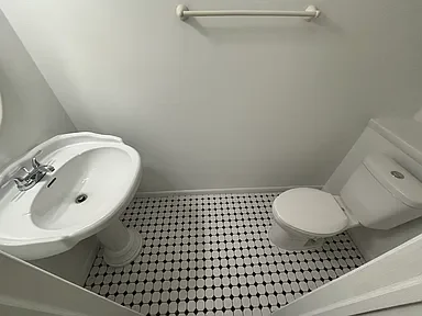 Small bathroom with a white toilet, a pedestal sink, and a towel rack on the wall, black and white tiled floor.