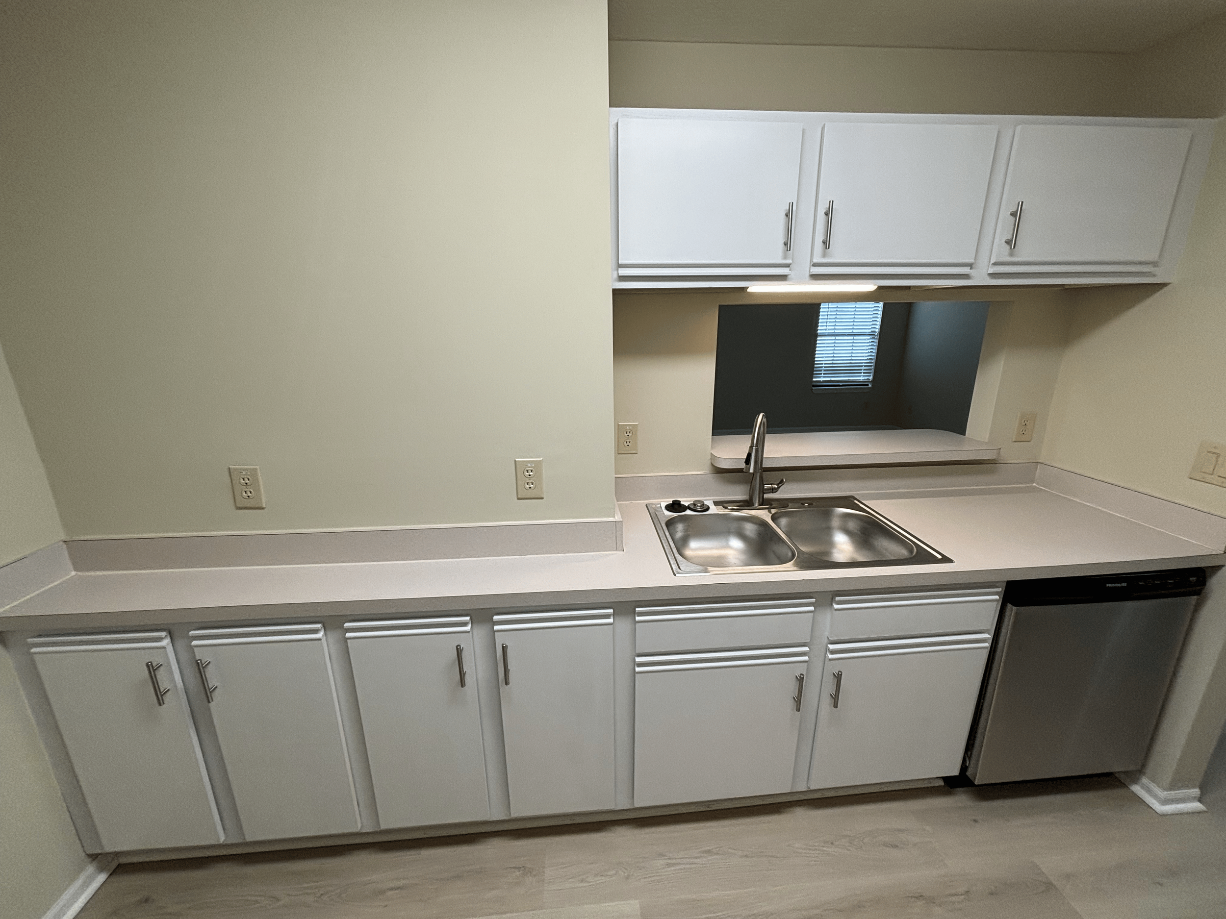 Kitchen with white cabinets, a stainless steel sink, a small dishwasher or refrigerator, and a cut-out window with a window in the background.