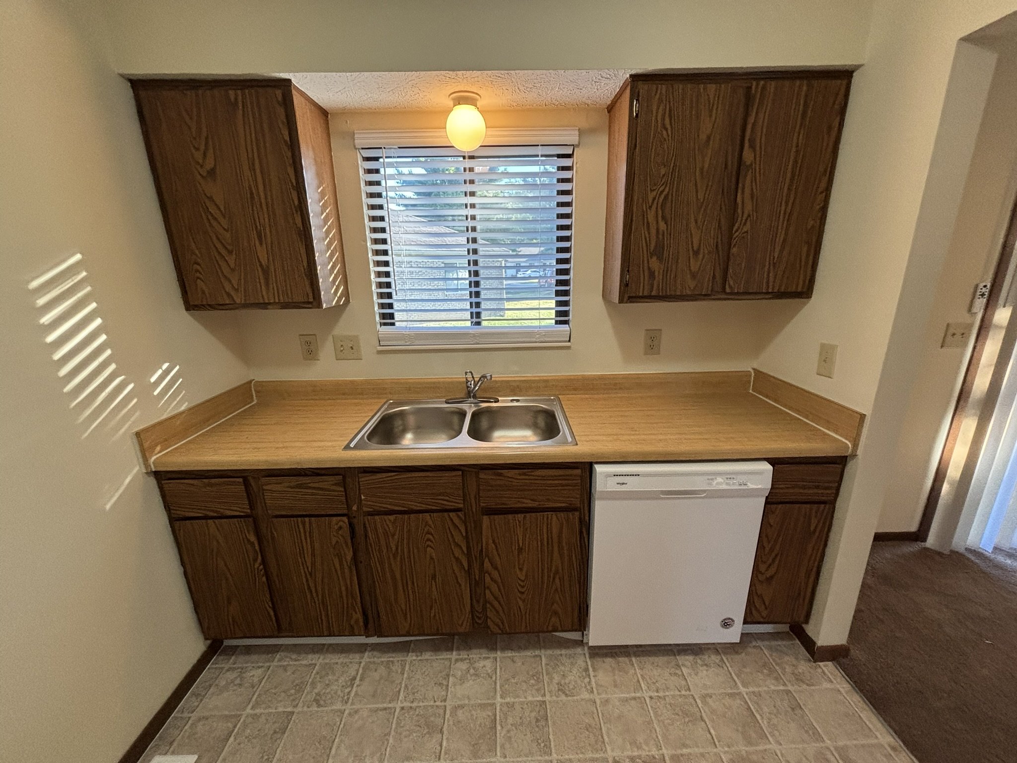Kitchen with wooden cabinets, a double sink, dishwasher, and a window with blinds