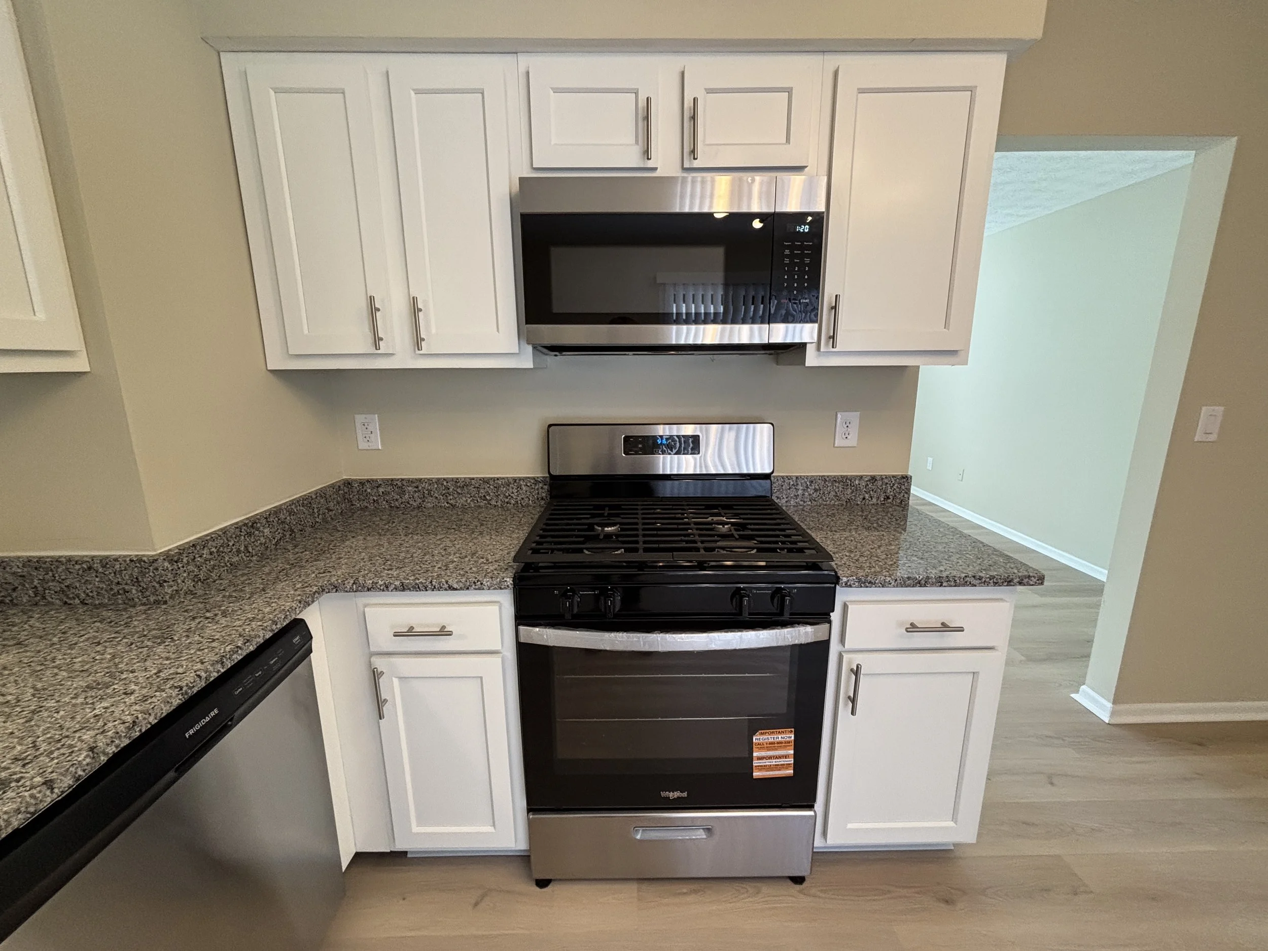 Kitchen with white cabinets, granite countertops, stainless steel microwave and stove, and a dishwasher. The scene shows part of the kitchen with a view into the adjacent room.