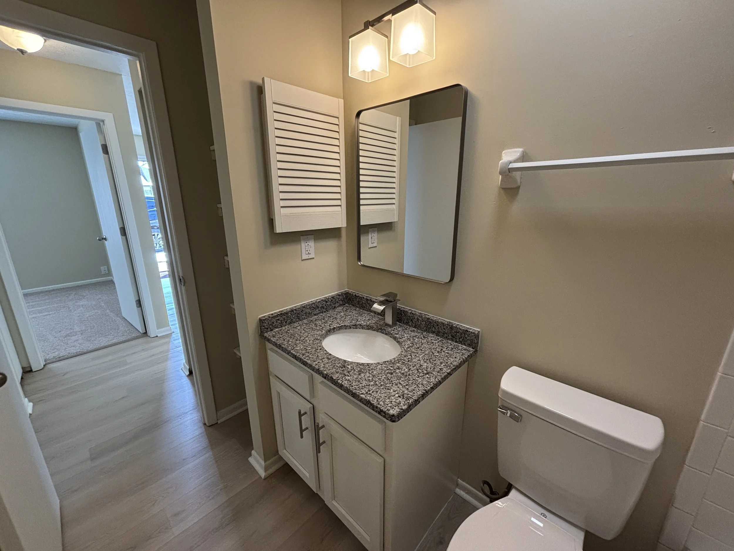 Bathroom with a granite countertop sink, mirror, wall-mounted cabinet, white toilet, towel bar, and towel cabinet, with a doorway leading to another room.