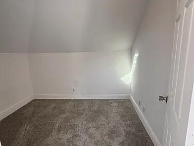 Empty room with white walls, gray carpet, and a white door.