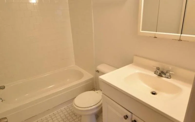 Small bathroom with a bathtub, toilet, and white sink with mirror above.