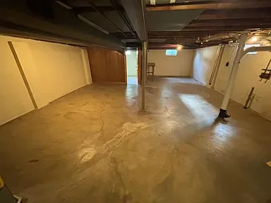 Empty basement with concrete floor, exposed pipes, and a support column.