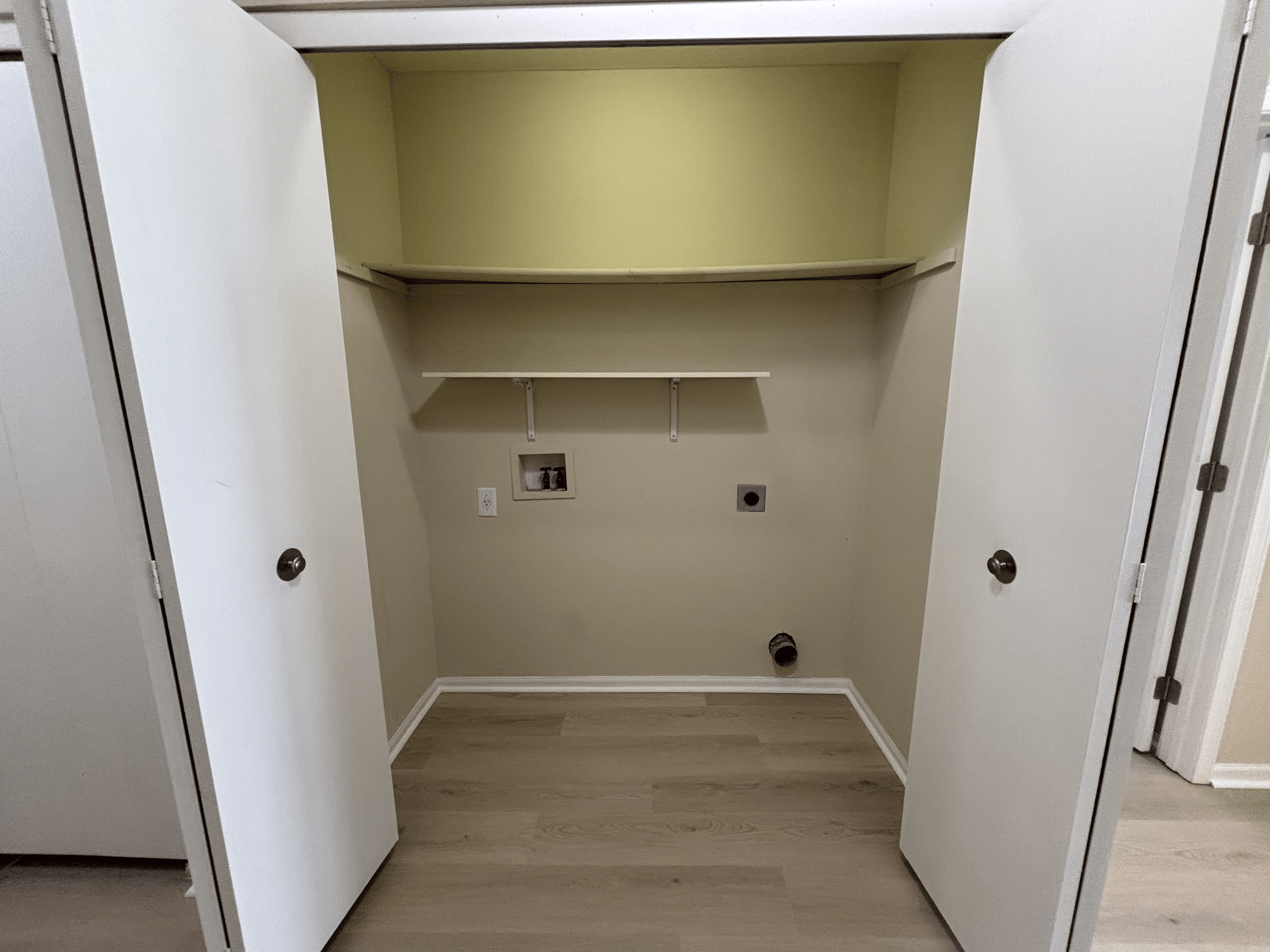 Empty laundry closet with shelves, utility hookups, and flooring.