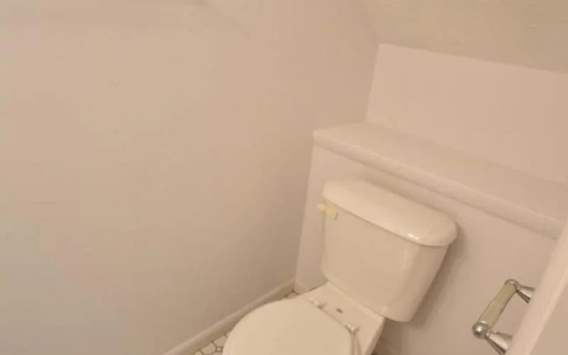 A white toilet in a small, corner bathroom with white walls and a tile floor.
