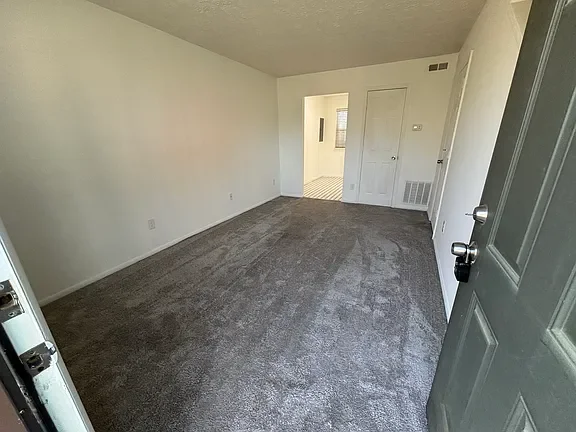 Empty living room with gray carpet, white walls, and an open doorway leading to another room.
