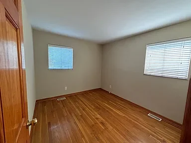Empty room with hardwood floors, two windows with blinds, and a closet door