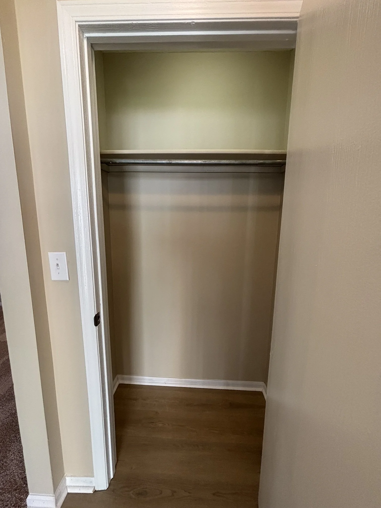 Empty closet with a wooden floor, beige walls, and a metal hanging rod.