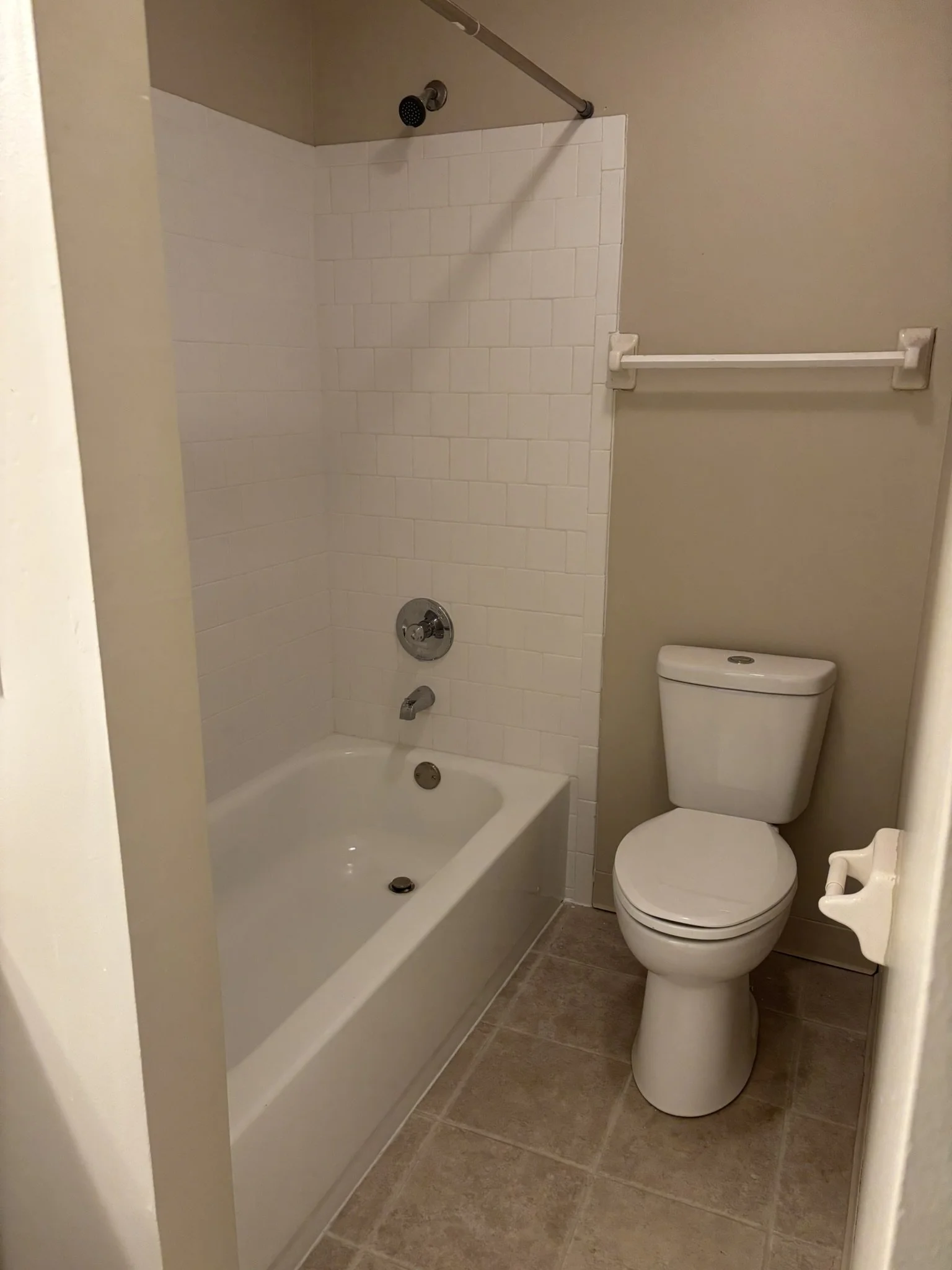 A small bathroom with a bathtub and shower, a toilet, and beige tile flooring.