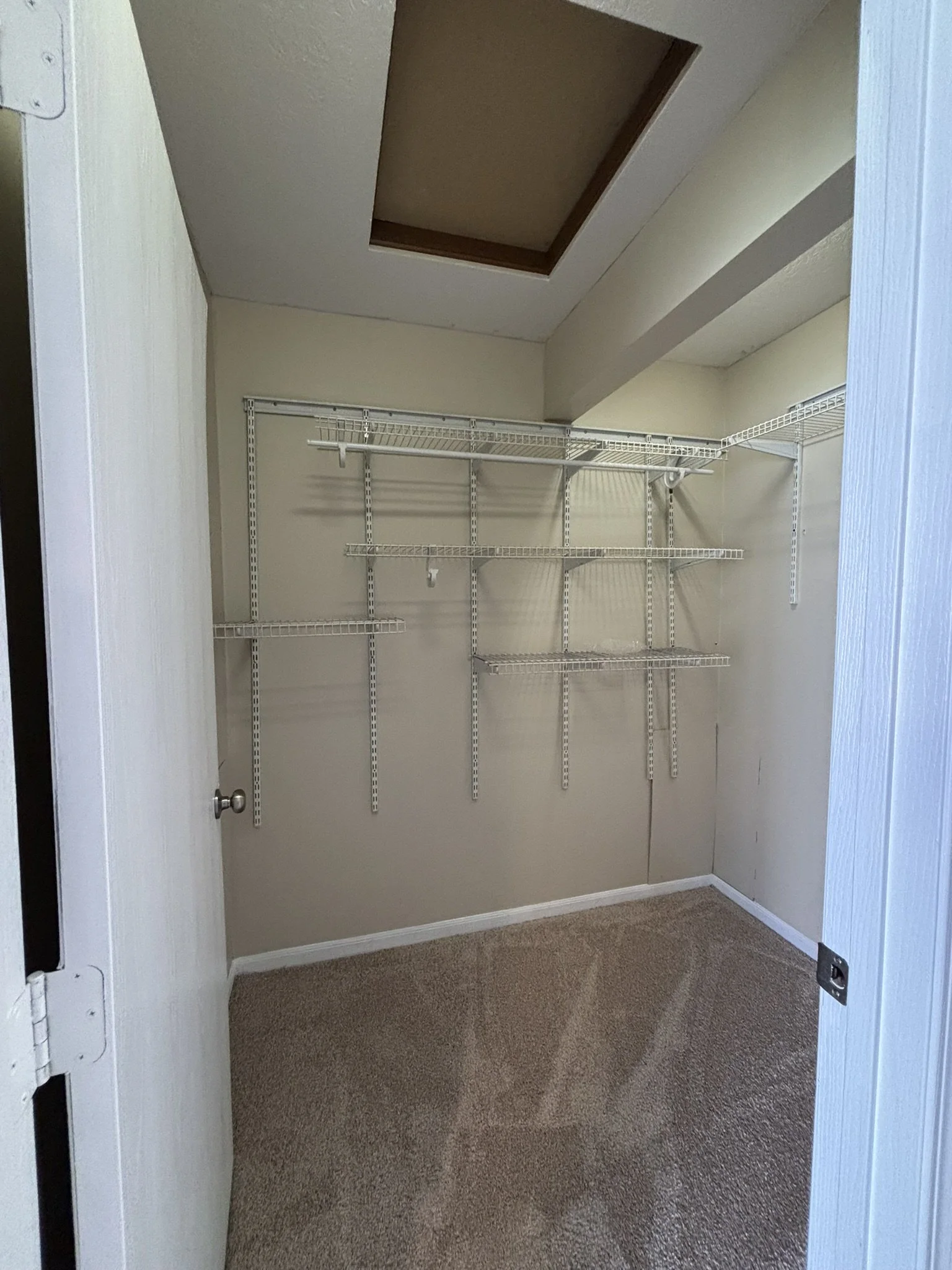 Empty walk-in closet with white wire shelving on beige walls and a small skylight in the ceiling.