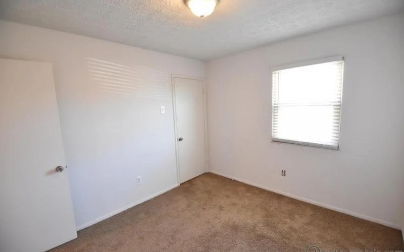 Empty room with white walls, a window with blinds, and an open door.