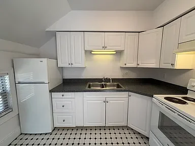 A small kitchen with white cabinets, a white refrigerator, a black countertop, a double sink, and an electric stove, with a black and white tiled floor.