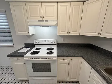 Kitchen with white cabinets, black and white checkered floor, gray countertop, and a white stove with four burners.