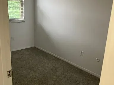 Empty room with beige carpet, white walls, a small window, and electrical outlets.