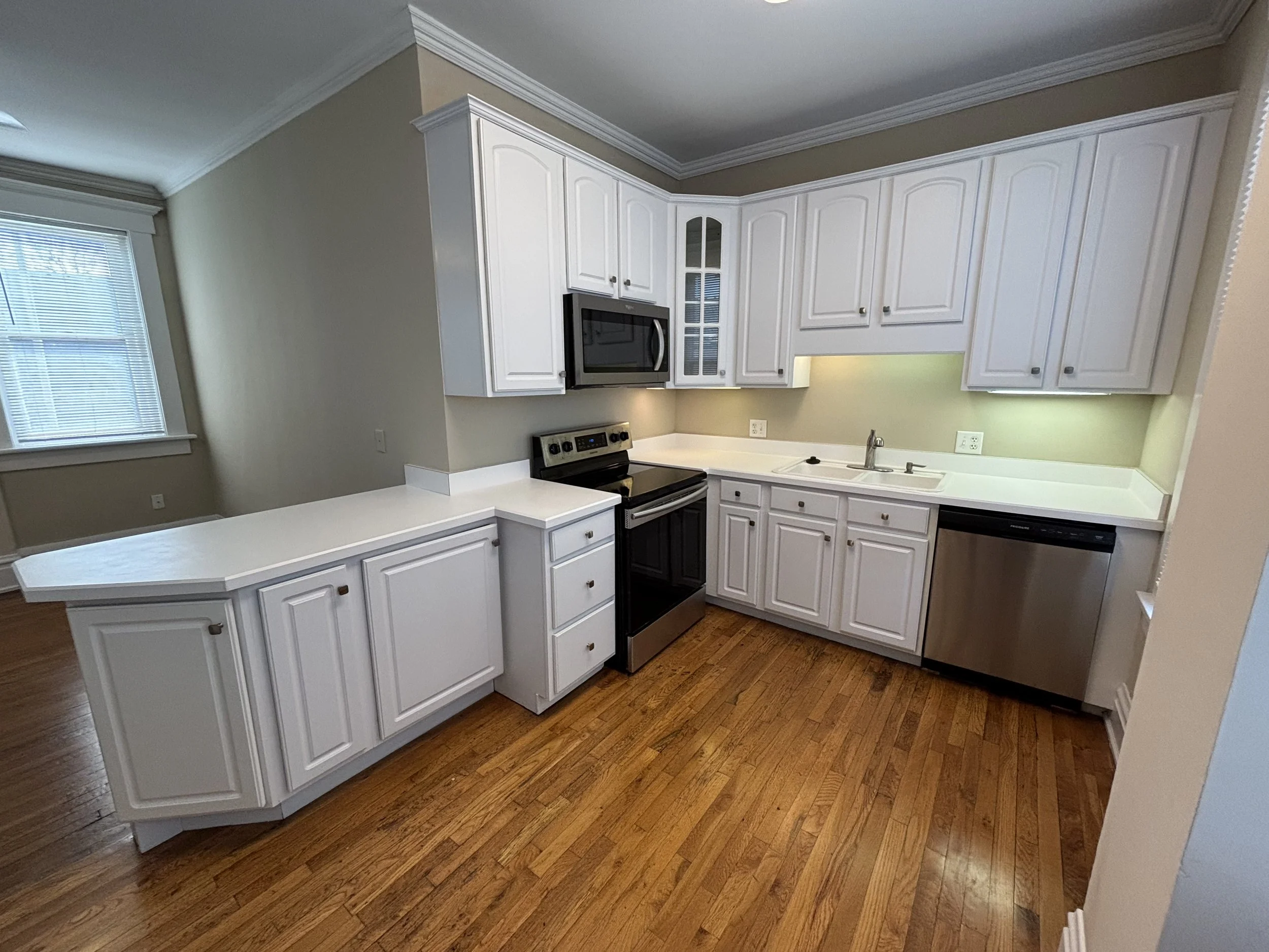 A kitchen with white cabinets, a black and stainless steel oven, microwave, dishwasher, and wooden flooring.