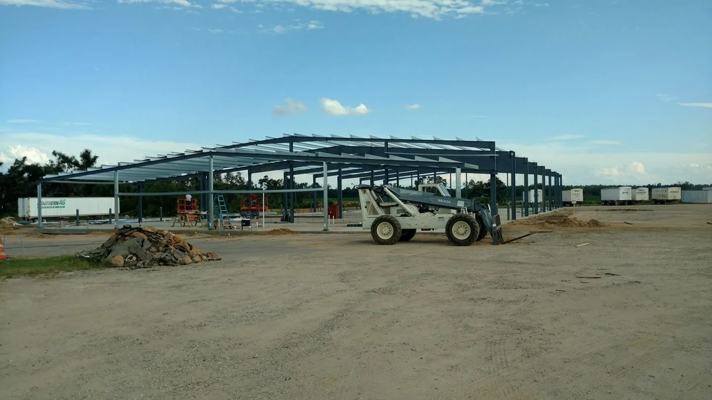 Construction site with a steel frame structure, construction equipment, and trucks in the background
