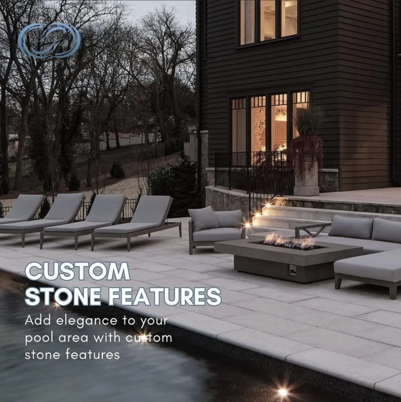 Outdoor pool area with lounge chairs, a fire feature, and stone features near a dark house at dusk.