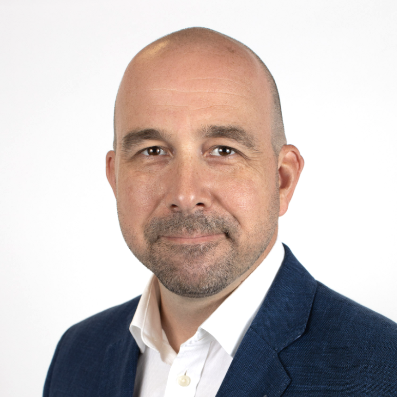 Professional headshot of a bald man with a beard, wearing a navy blazer and white shirt, against a plain white background.