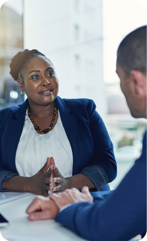 Two professionals having a serious conversation in a modern office, woman sitting with hands clasped, man listening attentively.
