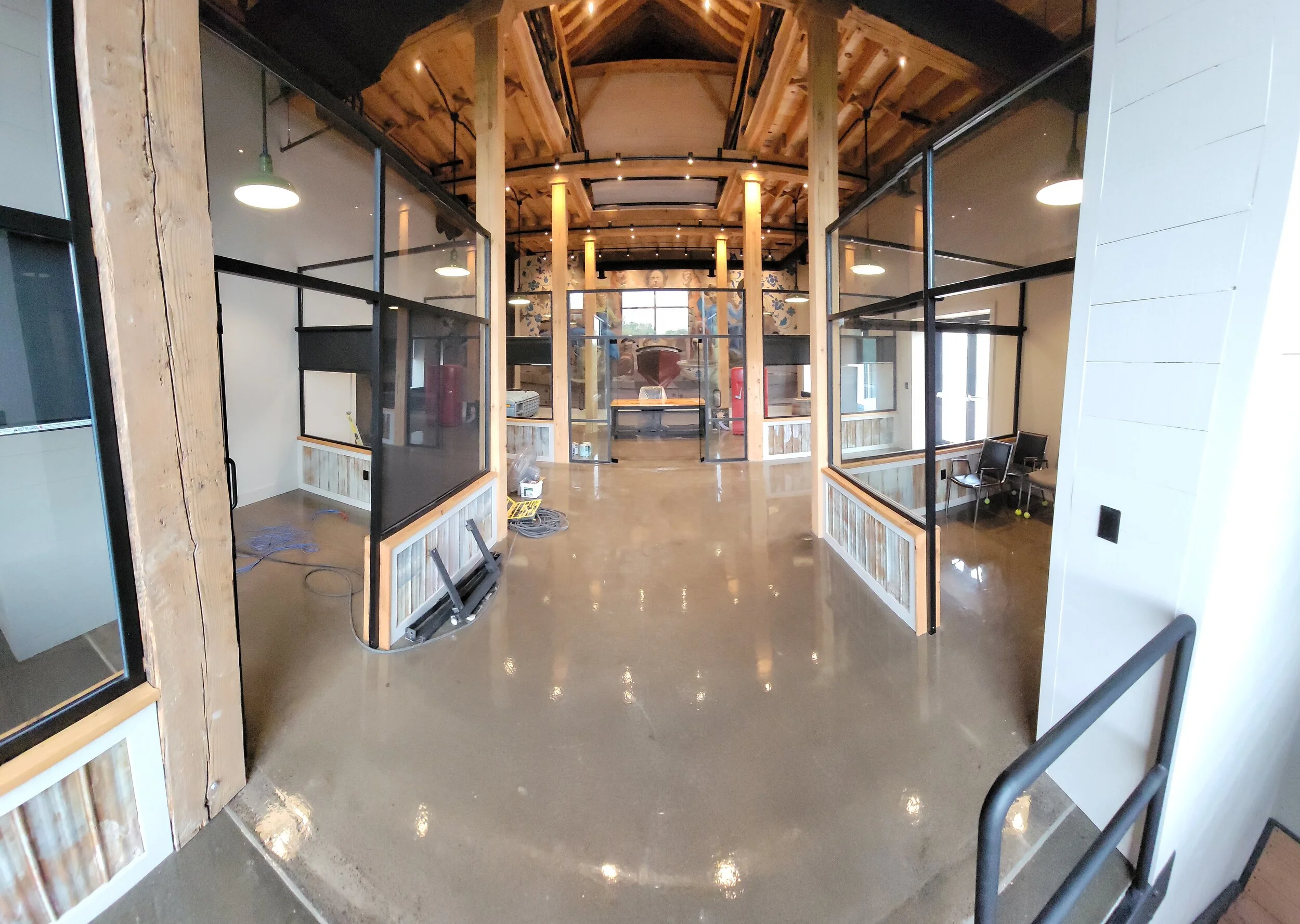 Interior of a modern commercial space with wooden framing, glass partition walls, polished concrete floors, and seating areas, under a high wooden ceiling.