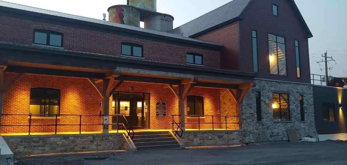 Exterior of a modern brick building with warm lighting, stone accents, and wooden support beams at the entrance, at dusk.