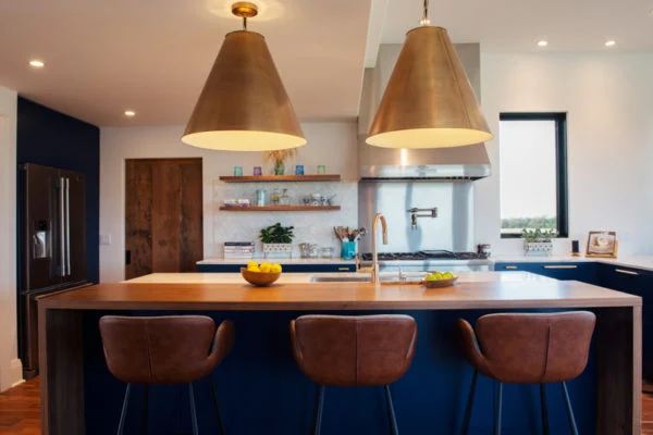 Modern kitchen with a large island, three brown bar stools, two pendant lights, open shelving, a sink, and a window with a view.