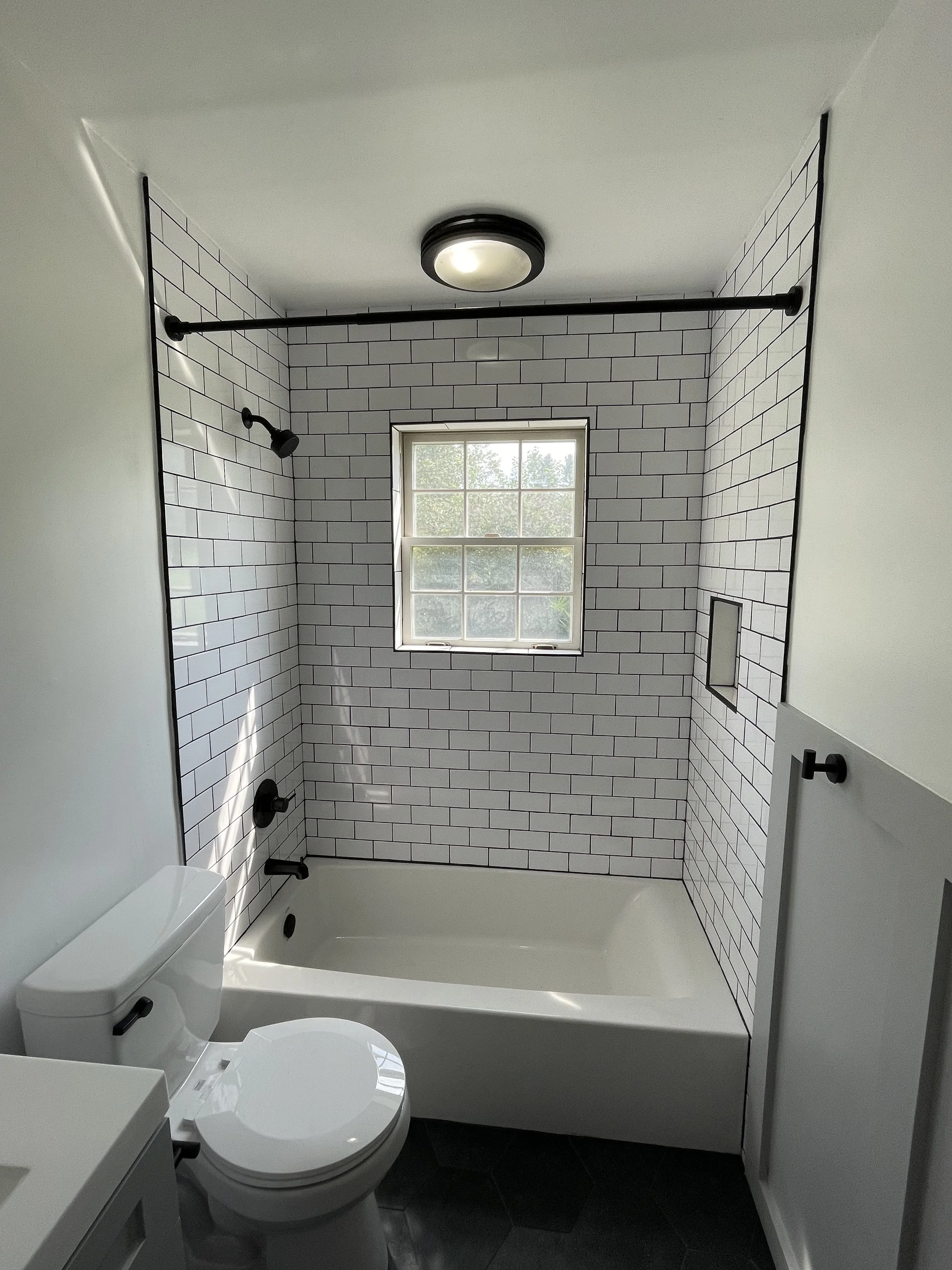 Bathroom with white subway tile walls, black fixtures, a small window, a bathtub, and a toilet.