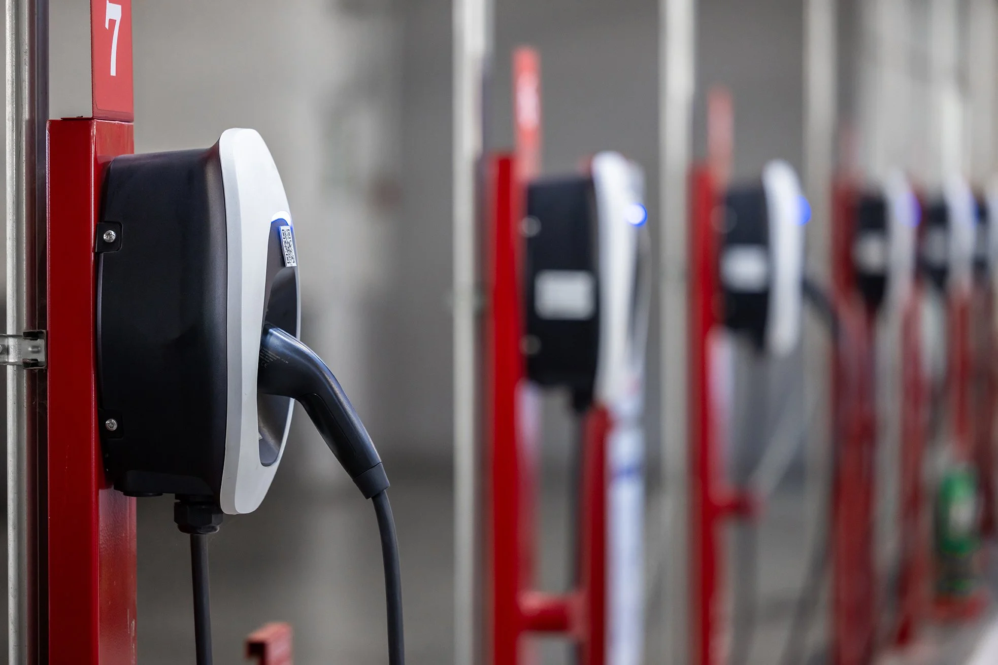Electric vehicle charging station with a charging cable plugged into an outlet, numbered 7, on a gray wall in a parking garage.