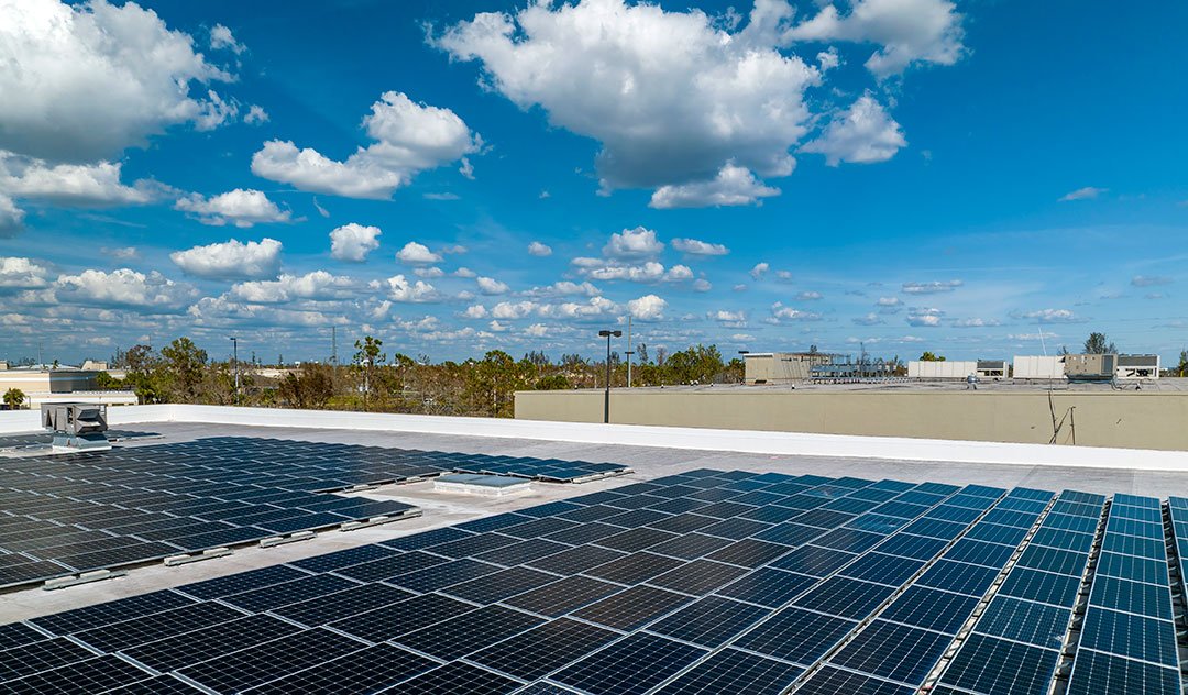 Solar panels on a building roof under a partly cloudy blue sky.