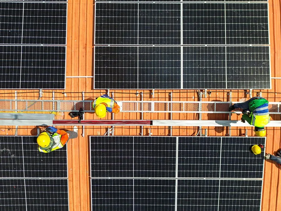 Workers wearing yellow safety helmets and reflective vests installing or maintaining solar panels on a rooftop.