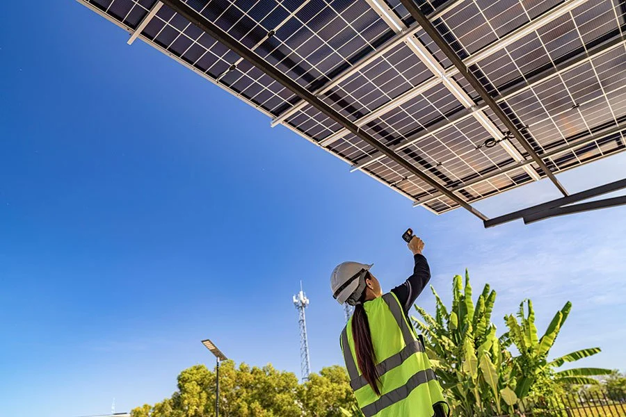 A woman in safety gear checking solar panels with a device outdoors.