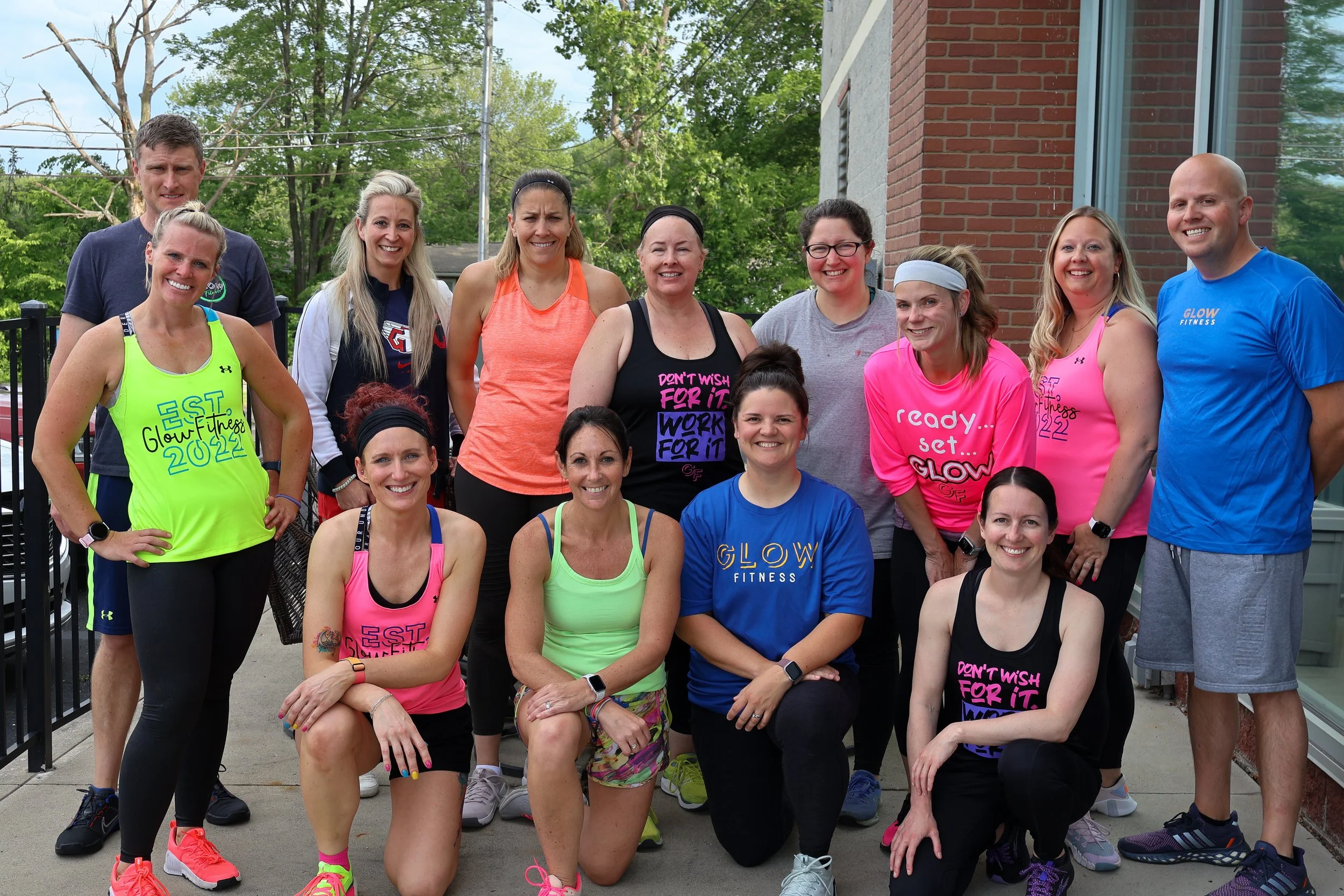 Group of people in athletic clothing posing outdoors in front of a brick building.