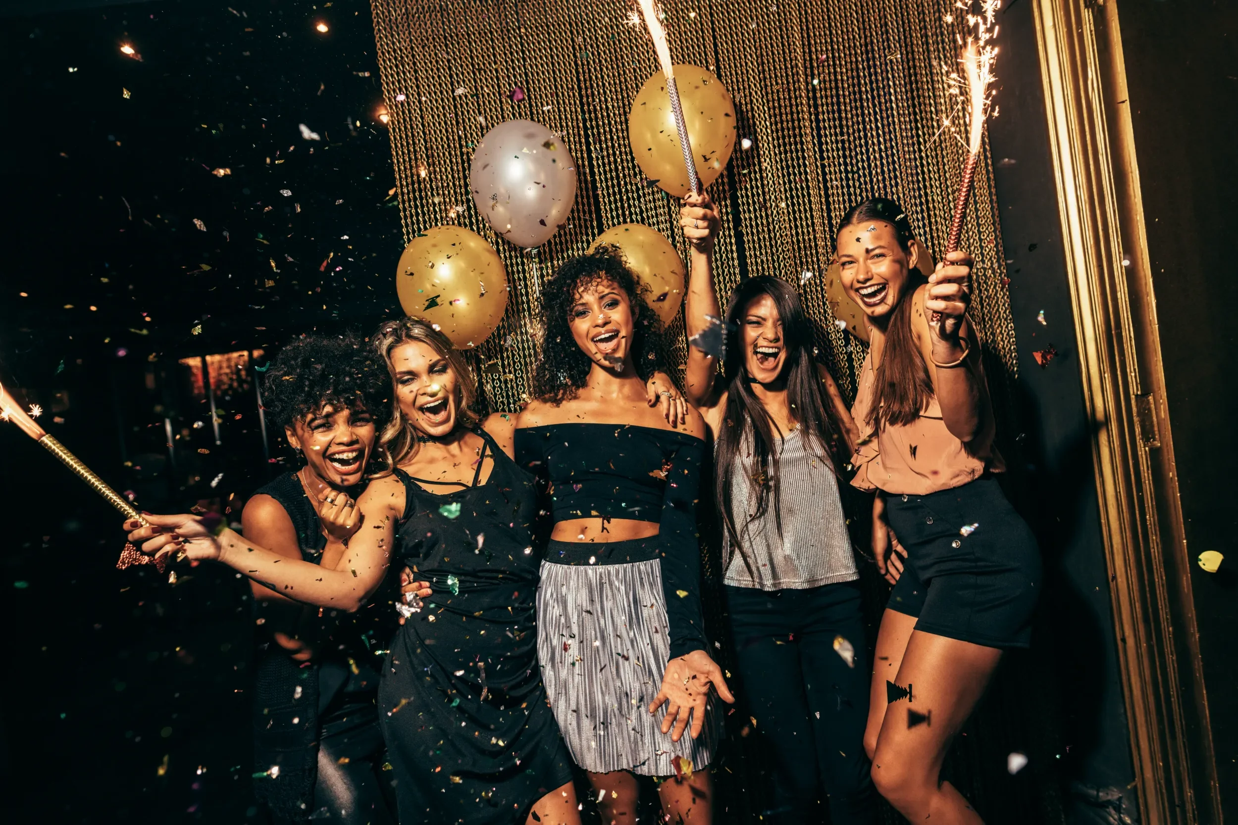 Group of happy & excited young women infront of decorated wall with confetti and balloons