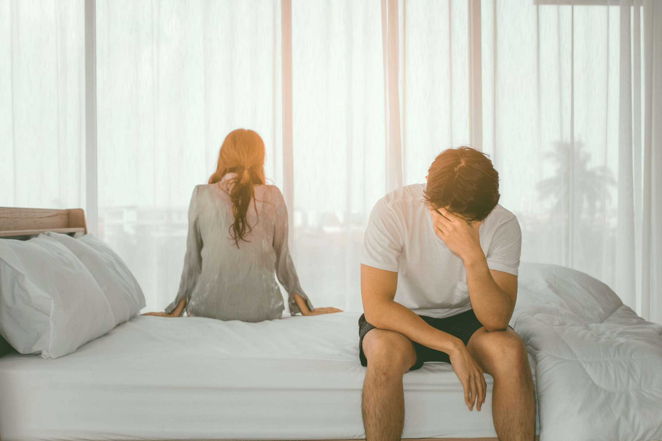 A couple sitting on opposite sides of the bed, a sign it's time for couples therapy