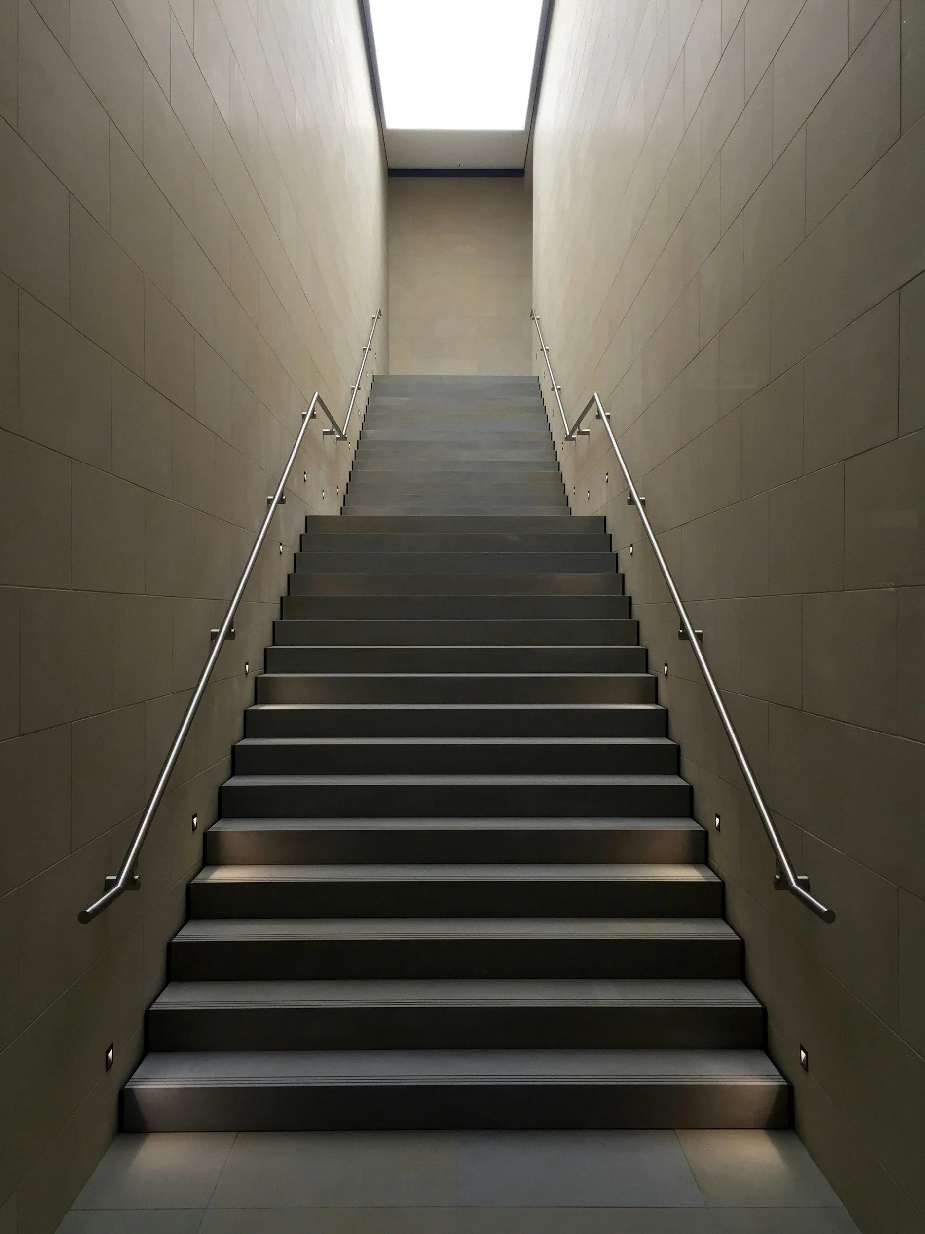 Modern indoor staircase with metal handrails, tiled walls, and recessed step lighting