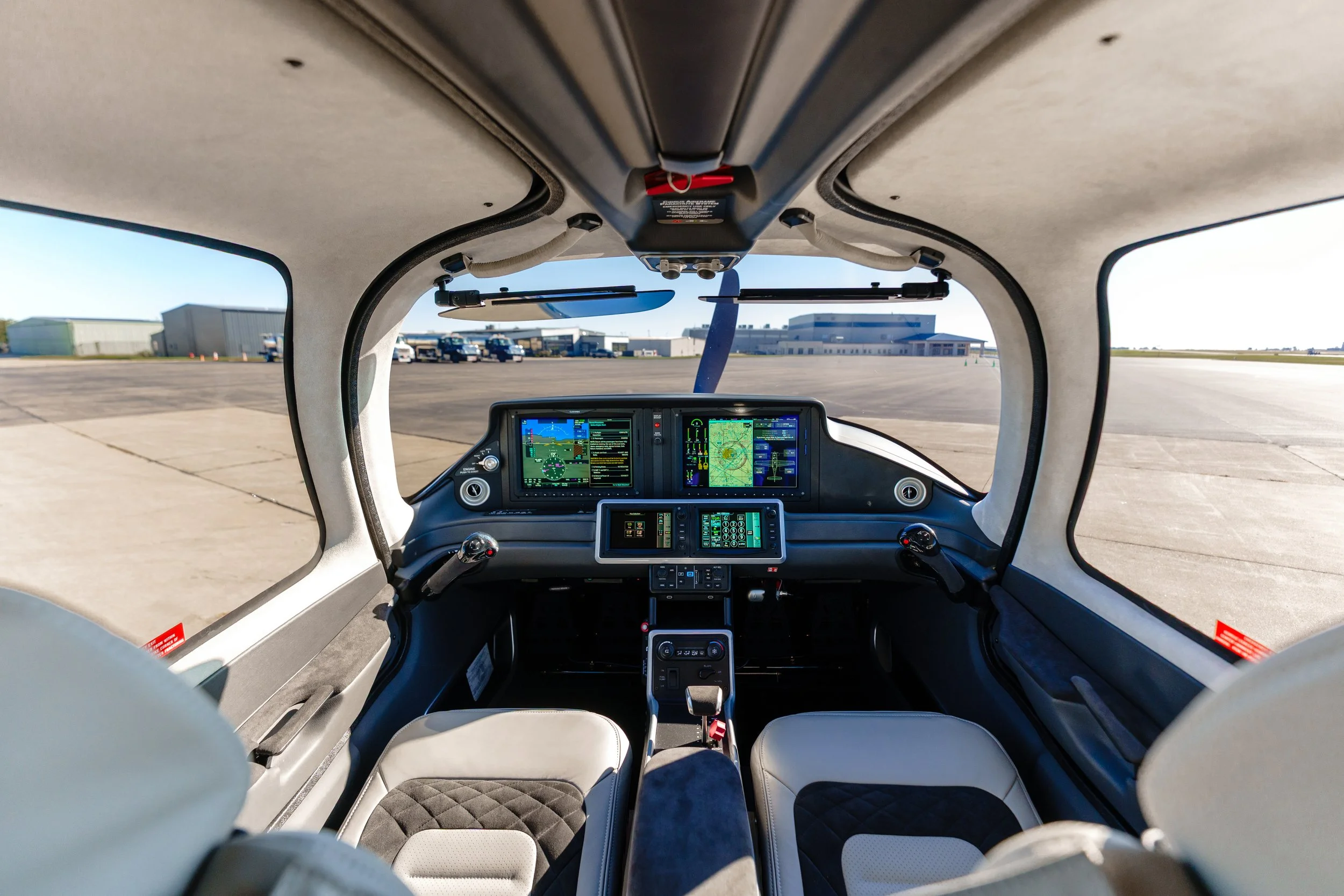 Wide interior view of a Cirrus aircraft cockpit showing the instrument panel, flight controls, and front seats.