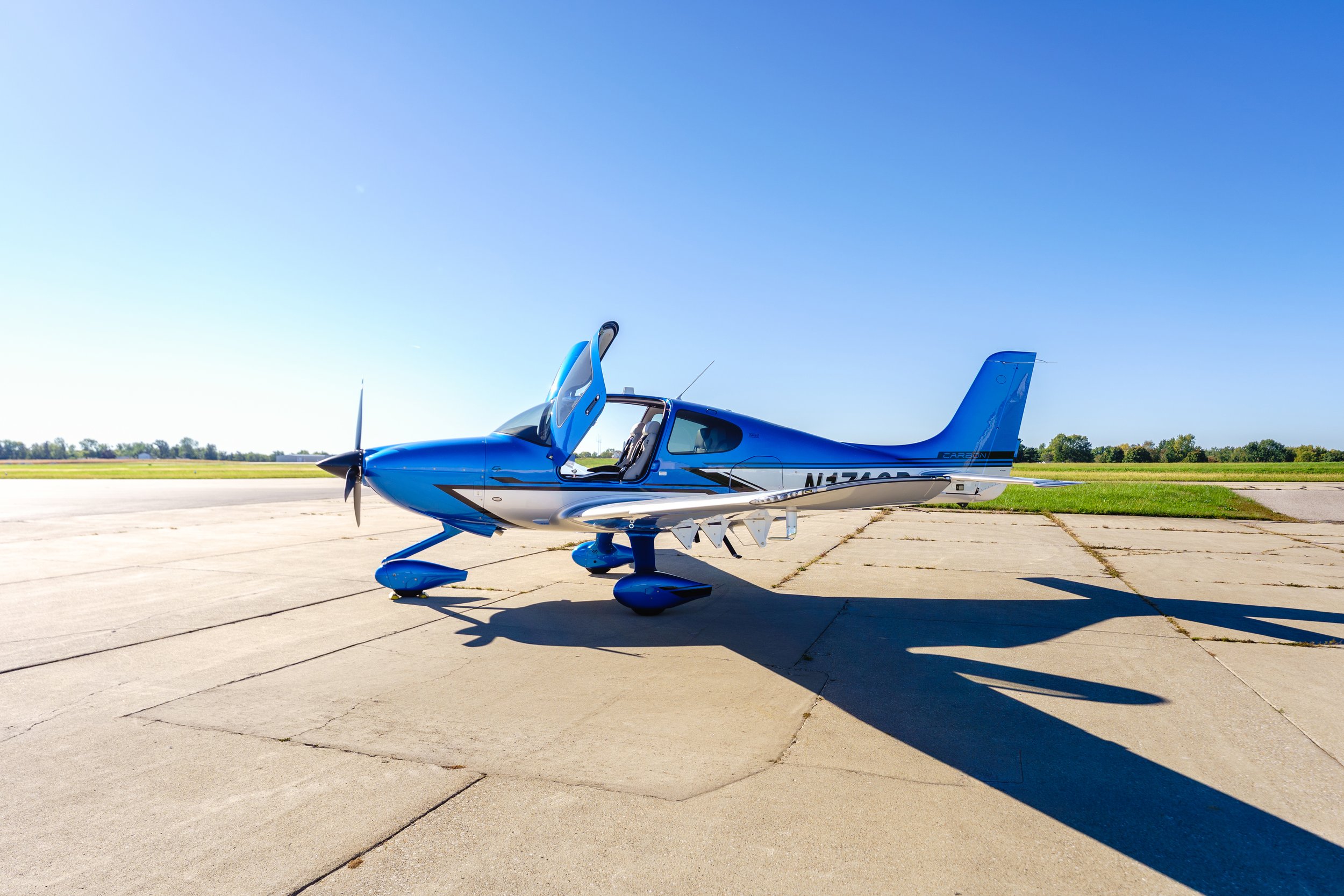 Side view of a blue Cirrus aircraft parked on the tarmac with its cabin door open.