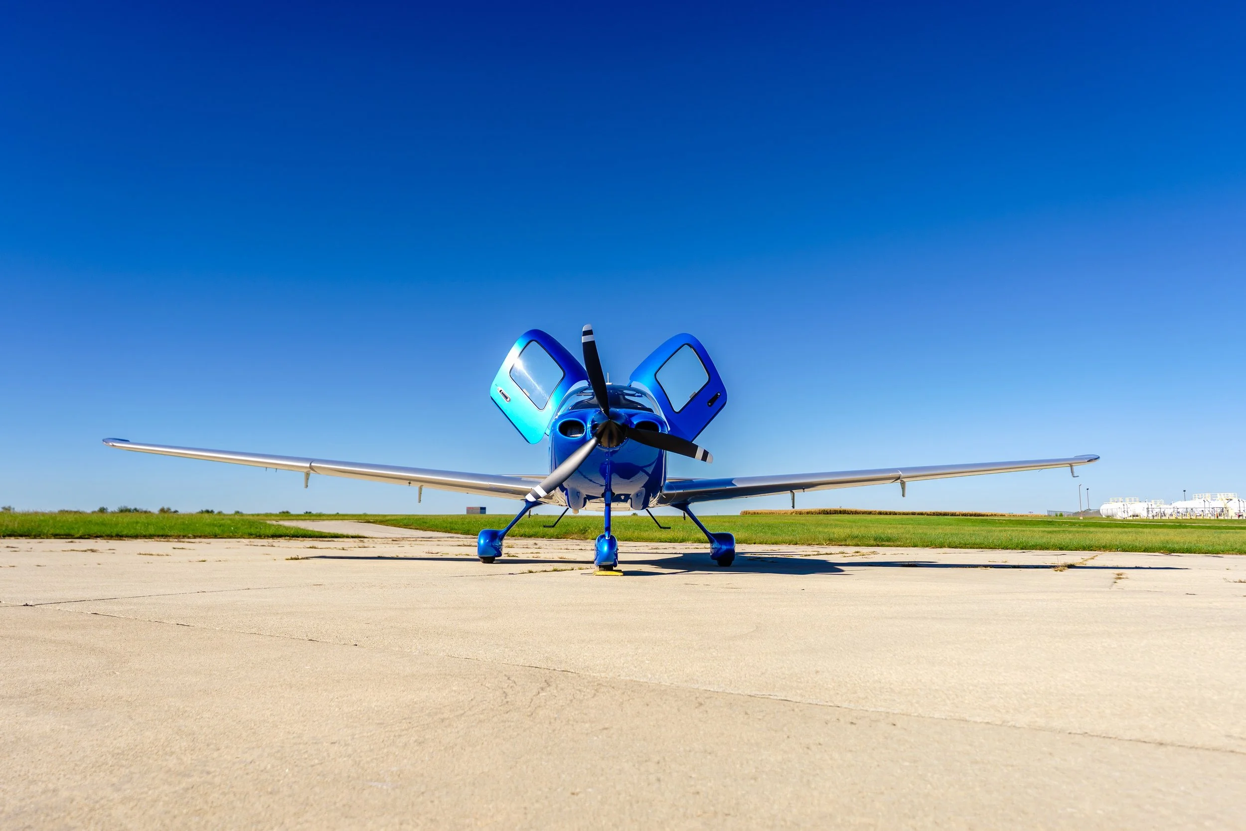 Front view of a blue Cirrus aircraft with both cabin doors open while parked on the tarmac.