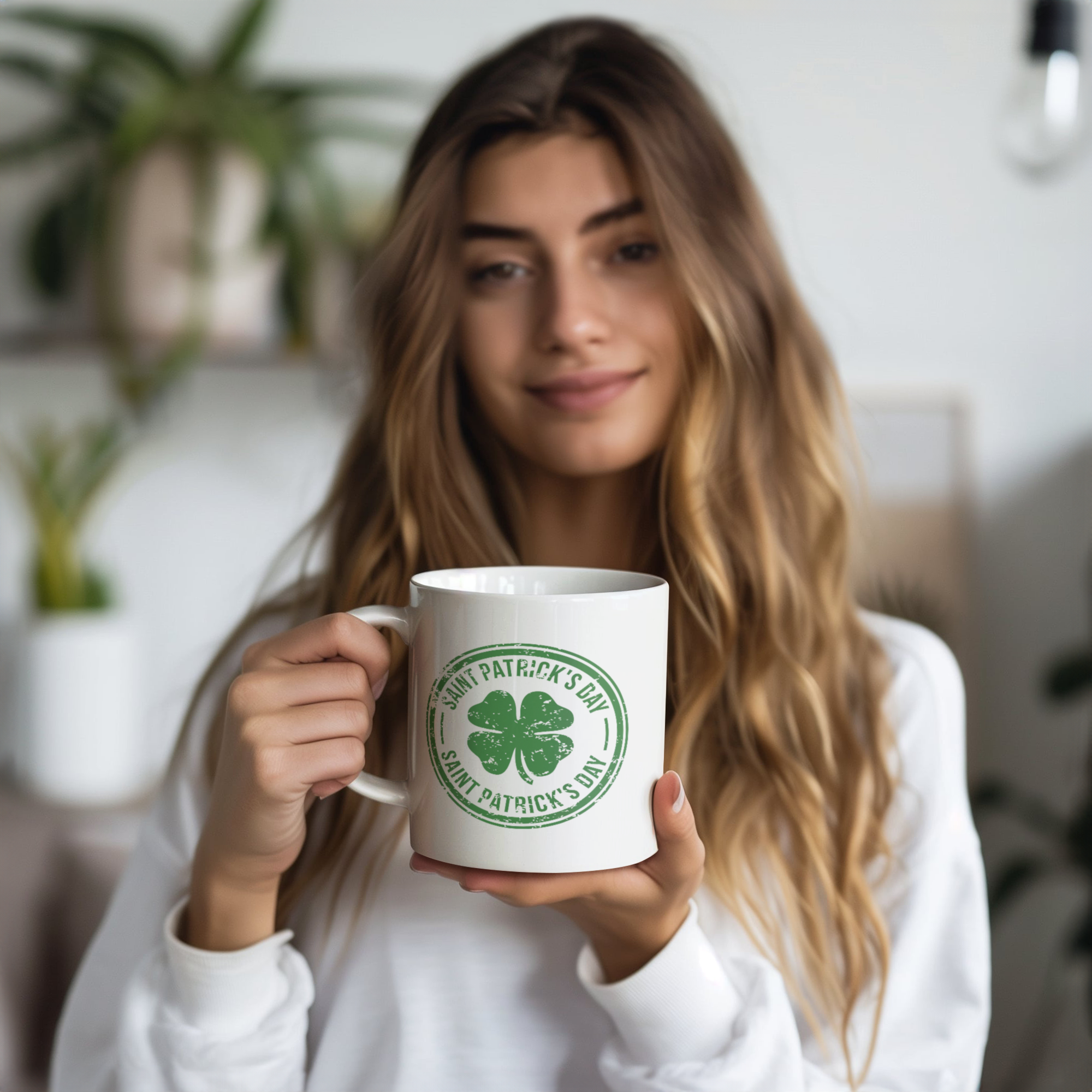 A woman with long light brown hair smiling and holding a white coffee mug with a Saint Patrick's Day logo featuring a green shamrock, in a bright indoor setting with a blurred background including green plants.