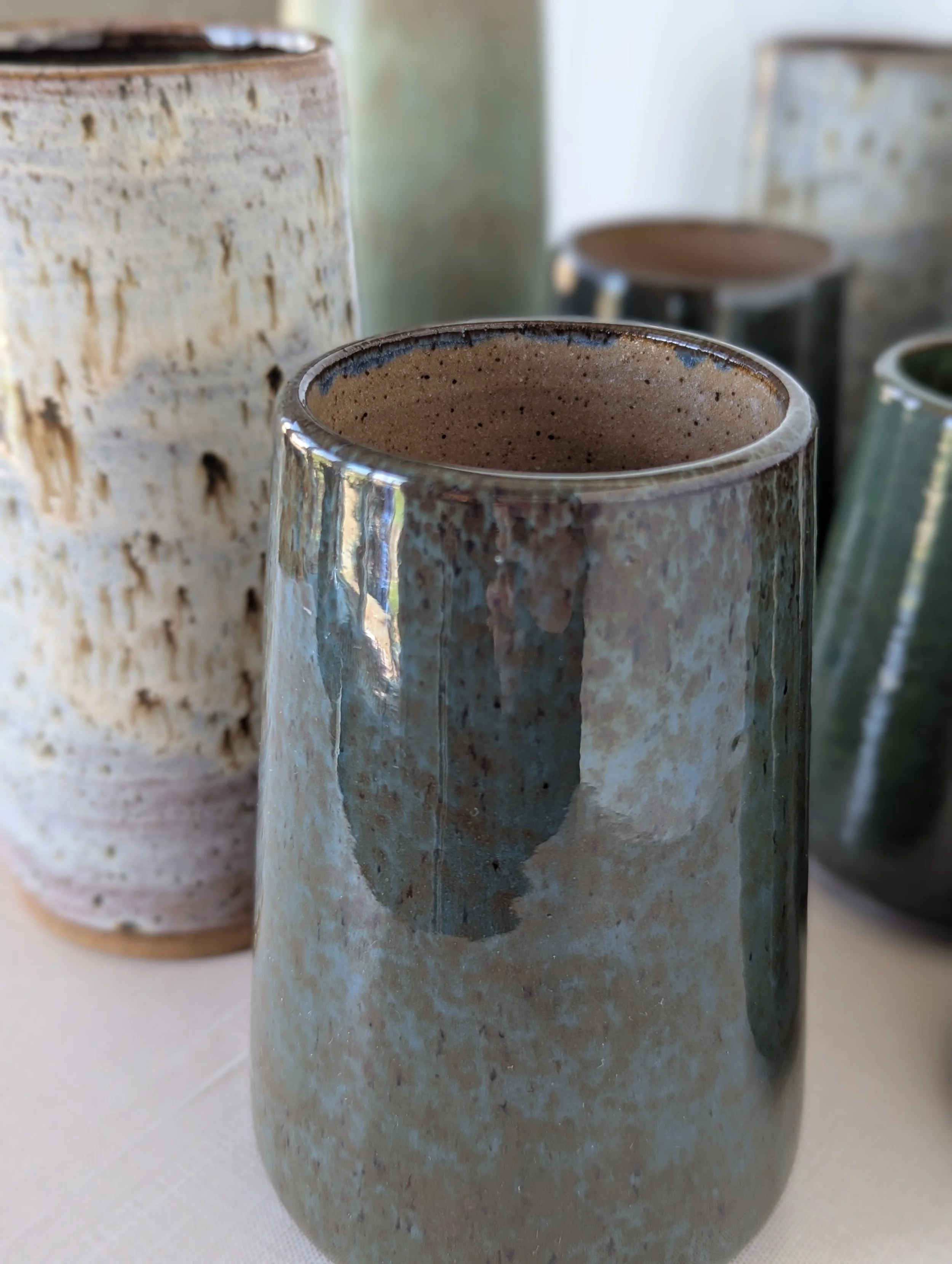 Close-up of a glazed ceramic vase with earthy tones, surrounded by other ceramic vases on display.