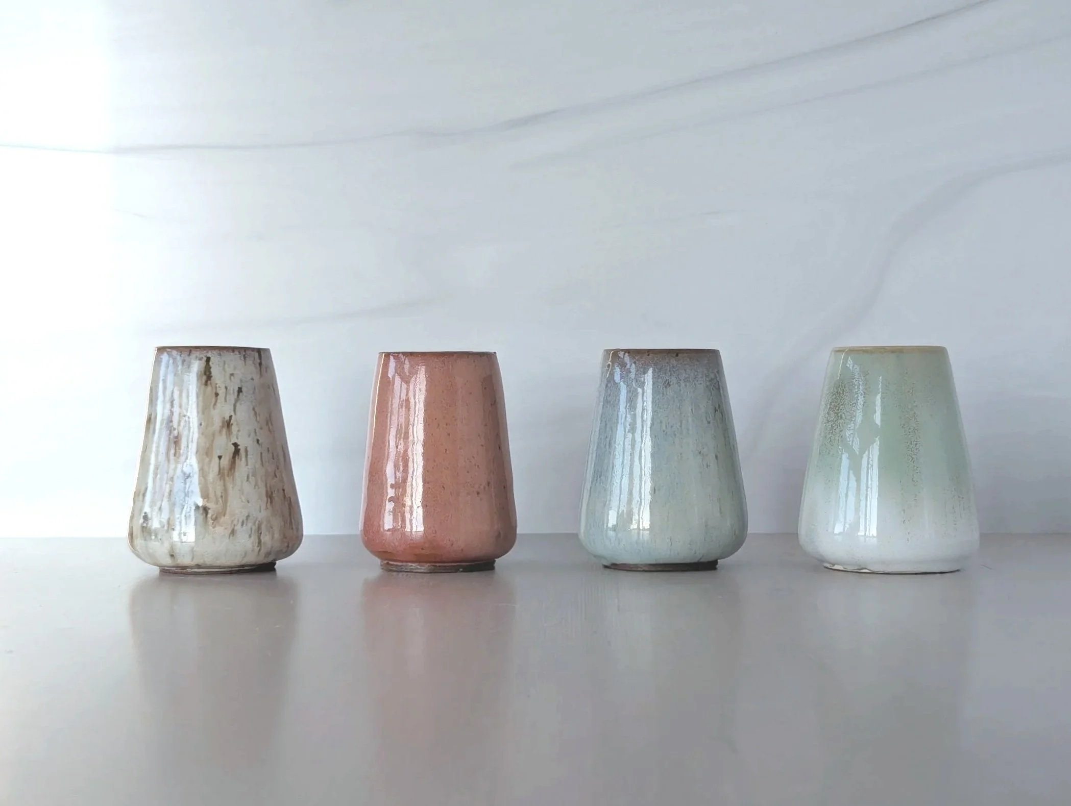 Four ceramic cups with a glossy finish placed in a row on a light-colored surface against a light background.