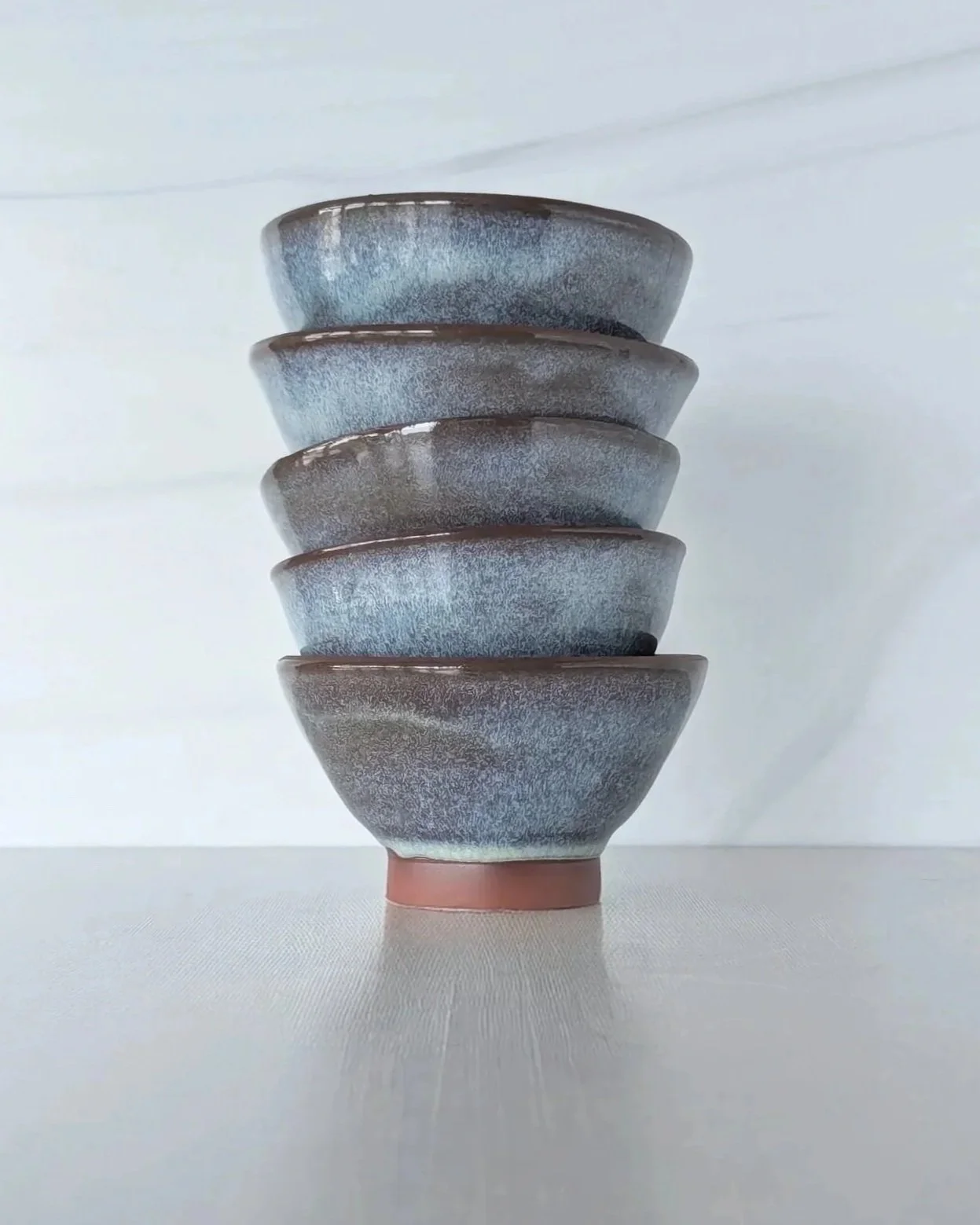 Stack of five ceramic bowls with a speckled gray and blue glaze, arranged on a white surface against a white background.